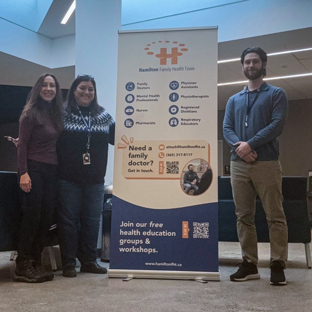 Three HFHT staff members smile at the camera while standing next to an HFHT banner at an outreach event.