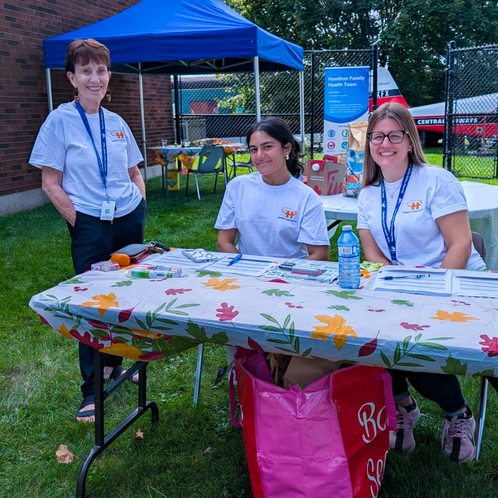 Three HFHT staff members smile at the camera at an outreach event at the Eva Rothwell Centre.