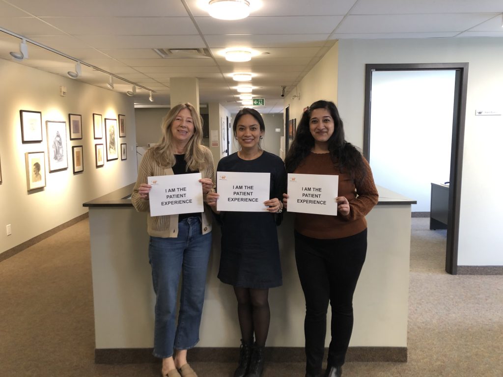 The HFHT finance team holds "I am the patient experience" signs and smiles at the camera.