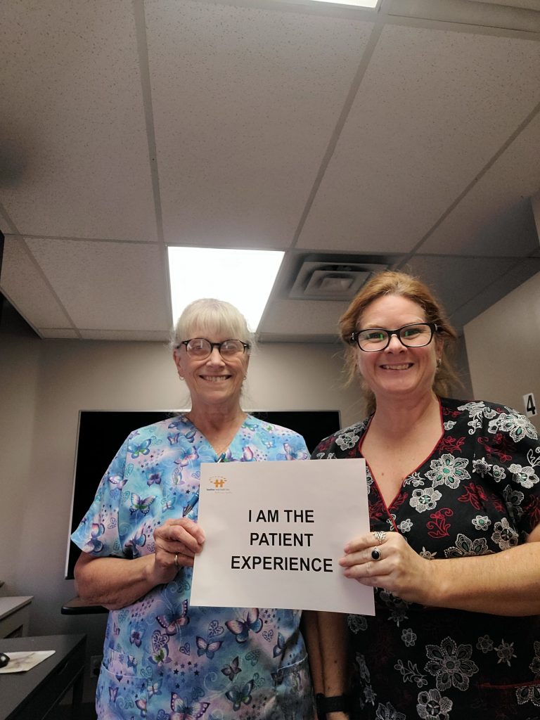 Dr. Alton’s Practice Team hold an "I am the patient experience" sign and smile at the camera.