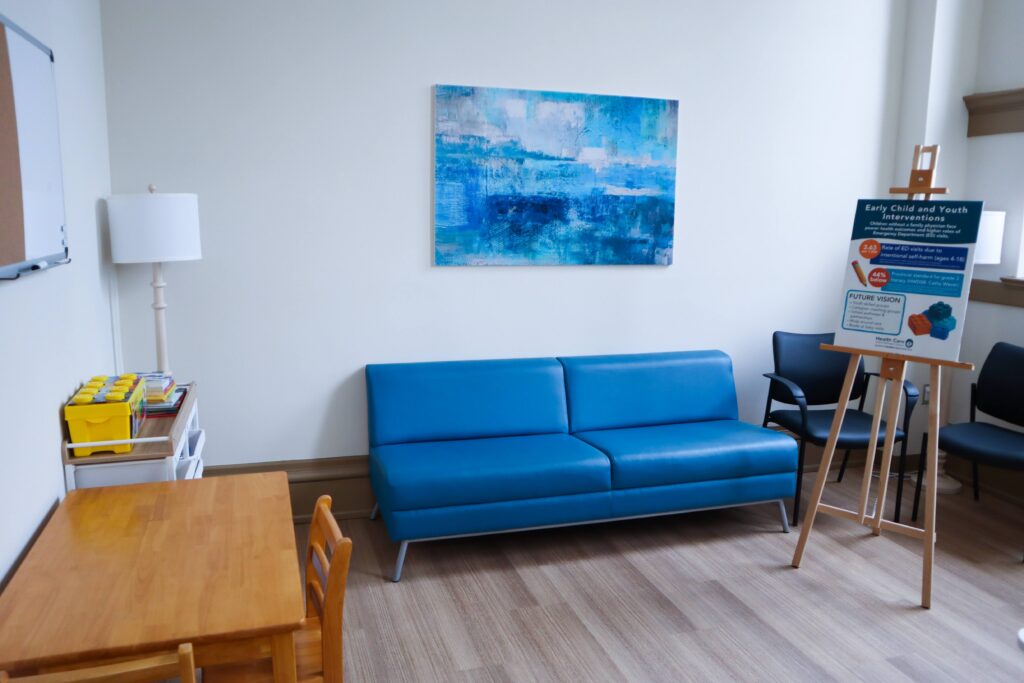 A room with a blue pleather couch, small table and print on the wall.