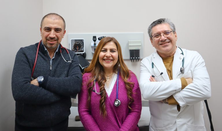 Three family doctors wearing stethoscopes smile at the camera.