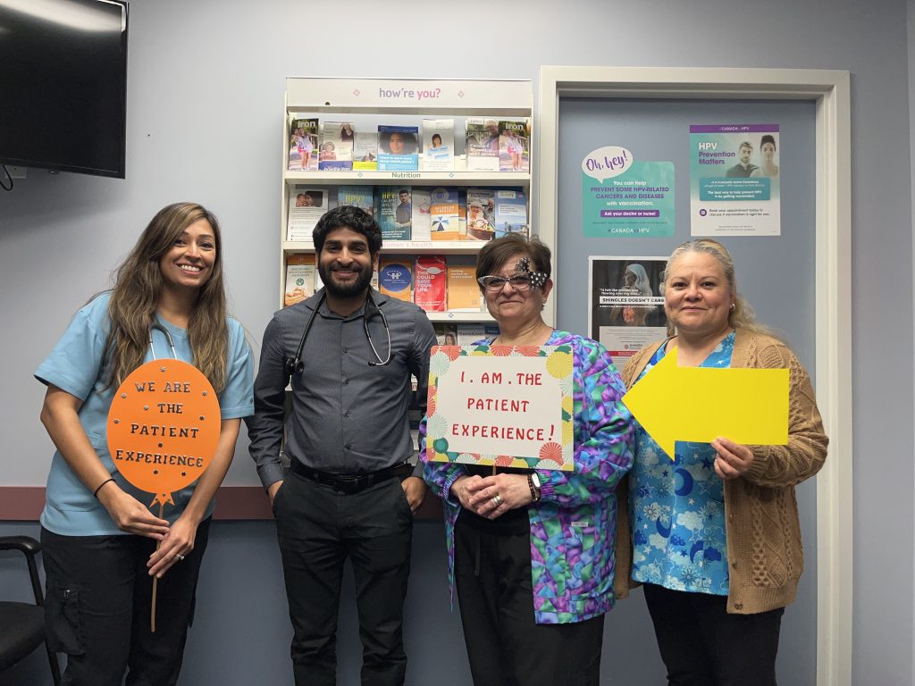 Dr. Brendan L.C. Singh’s Practice Team holding up colourful 'I am the patient experience" signs and smiling at the camera.