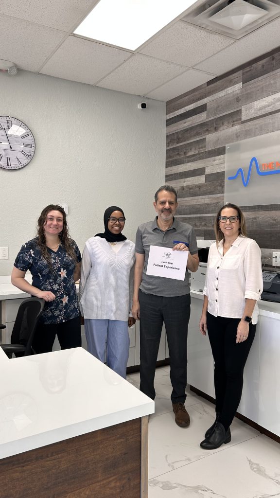 Dr. Michael’s Practice Team hold an "I am the patient experience" sign and smile at the camera.