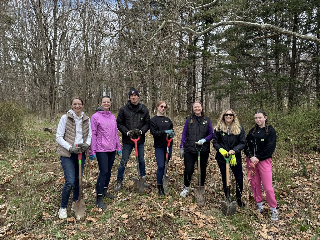 A group in a forest, some posing with shovels.