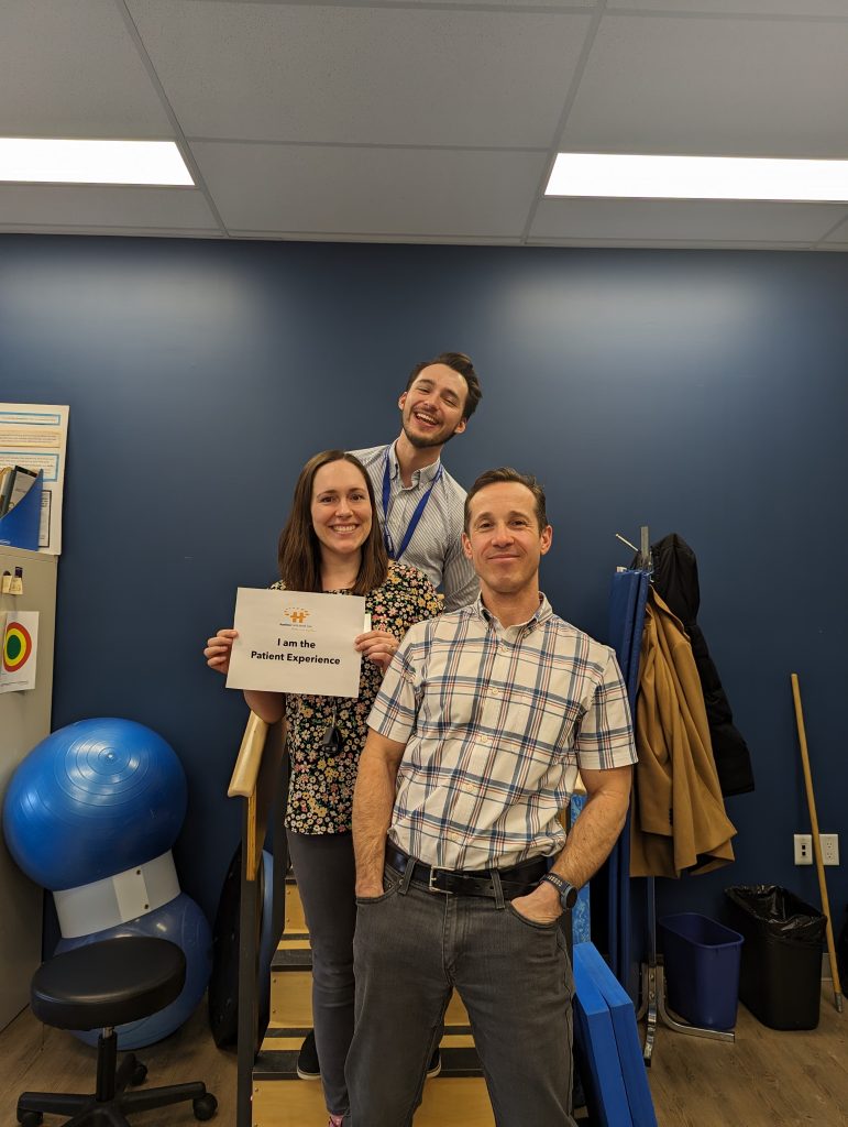 HFHT's physio team holds an "I am the patient experience" sign and smile at the camera.