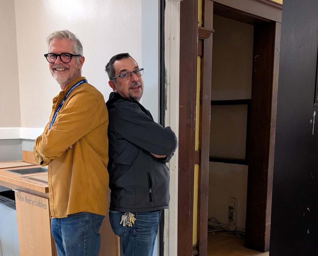 Two people, crossing their arms facing back-to-back, wearing glasses.