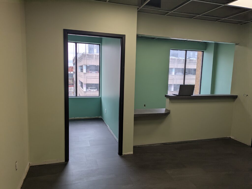 A room with dark floors, tan and teal walls, and windows.
